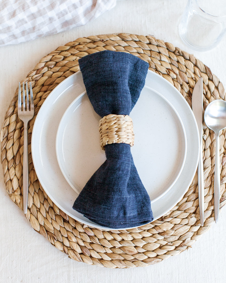 water hyacinth napkin ring around navy blue linen napkin on water hyacinth charger