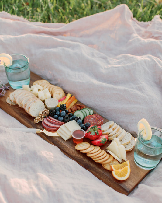 wooden board cheese board on pink linen blanket picnic