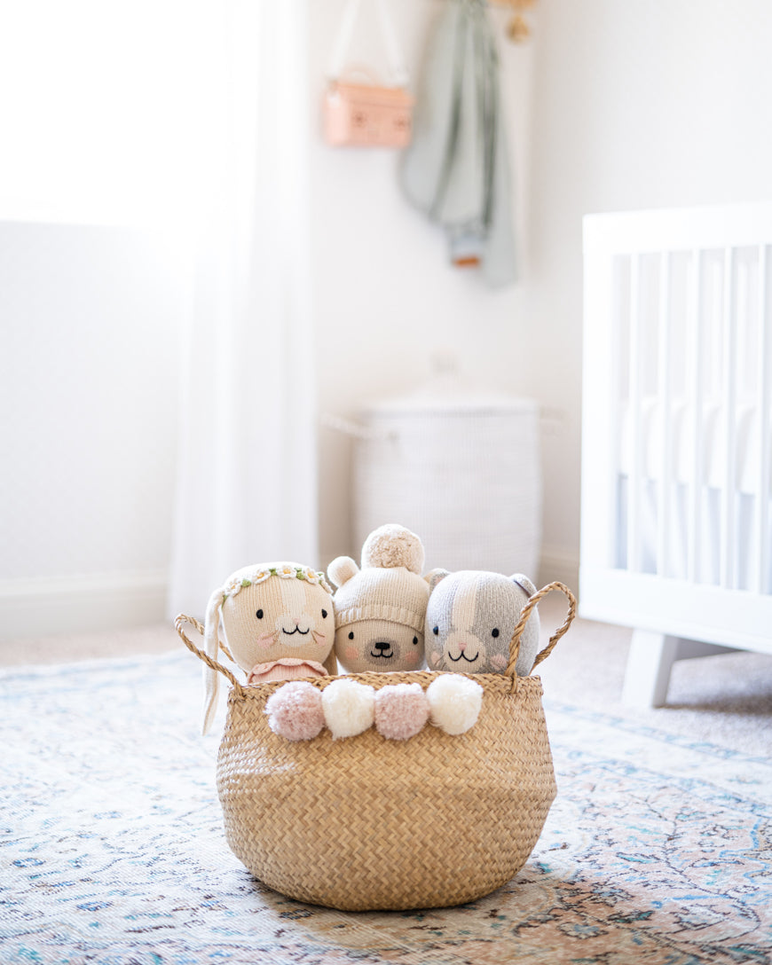 woven basket with poms filled with stuffed animals in a nursery